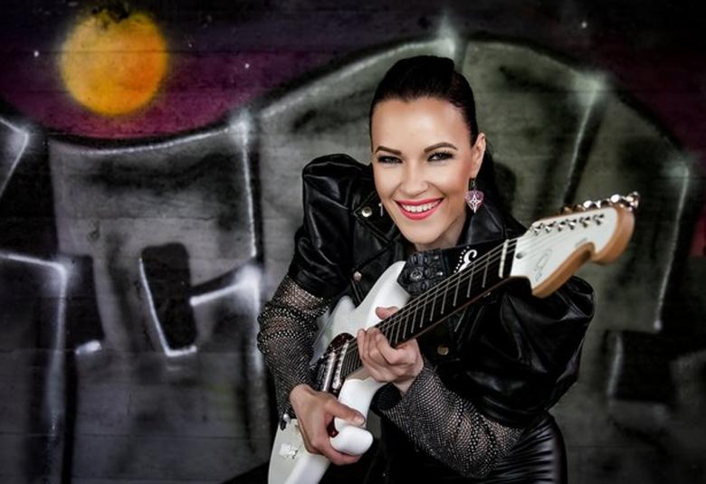 Kuvassa on Erja Lyytinen valkoinen kitara kädessään puolivartalokuvassa. Taustalla mustia koukeroisia kirjaimia ja yläpuolella himmeä keltainen kuu.