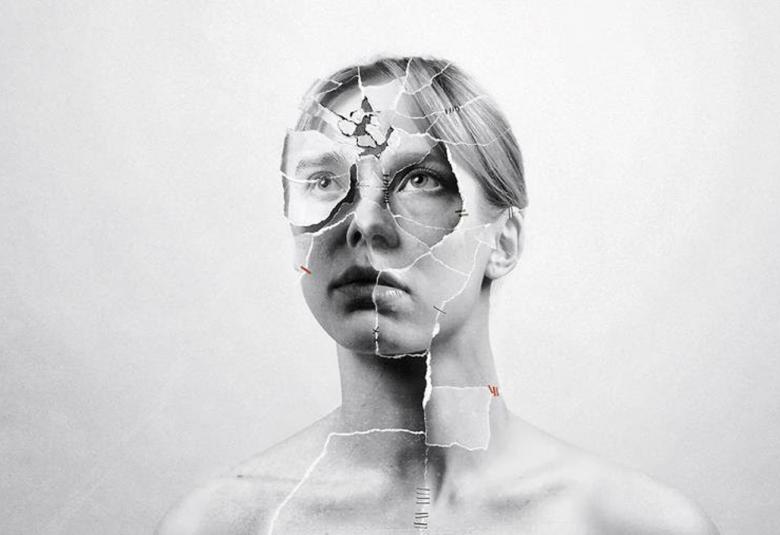 Kuvassa on nuoren naisen kasvot ja niissä on lasimaisia murtumia. Kuvassa näkyy osittain hartioita. Kuva on musta-valkoinen.