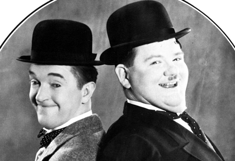 Kuvassa ovat vasemmalla Stan Laurel ja oikealla Oliver Hardy kasvokuvissa mustat hatut päässään. He ovat ruudutetun ympyrän sisällä ja hymyilevät.