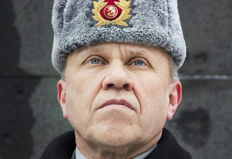 Kuvassa on Martti J. Kari kasvokuvassa ja hänellä on Suomen armeijan karvahattu, jossa on Suomen leijonan kokardi hatussa. Hattu on harmaa. Tausta on tumman harmaa.