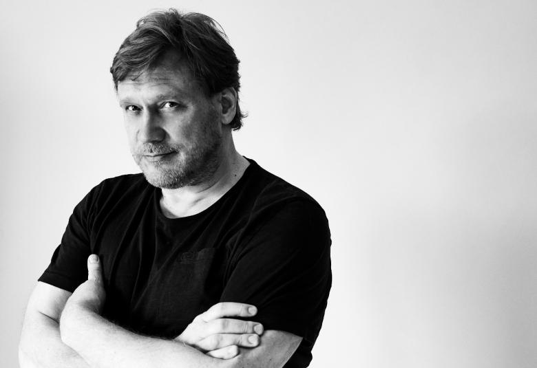 Kuvassa on Samuli Edelmann puolivartalokuvassa mustassa lyhythihaisessa t-paidassa.  Hänellä on kädet vedettynä rinnan yli kainaloihin ja hän seisoo kuvan vasemmassa reunassa.