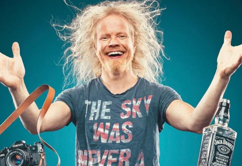 Kuvassa on Ville Juurikkala puolivartalokuvassa ja hänellä on sininen t-paita, jossa lukee The sky was never. Hänen kätensä ovat ohjennettuna sivulle ja hänen vaaleat hiuksensa harottavat.  Vasemmalla on ilmassa järjestelmäkamera ja oikealla viskipullo. Tausta on sininen.