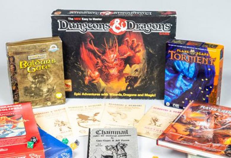 Kuvassa on keskimmäisenä Dungeons & Dragons -pelin paketti, jonka kannessa on punaisen lohikäärmeen kuva.  Ympärillä on on muita erilaisia pienempiä pelipaketteja ja pöydällä on kirjoja.