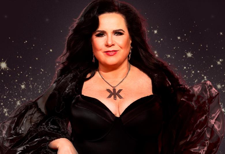 Kuvassa on Kaija Koo istumassa ja hänellä on on  musta avokaulainen puku ja kaulassaan koru, jossa on iso k symmetrisesti molempiin suuntiin. Tummat hiukset ovat hajallaan molempiin suuntiin. Taustalla on tummaa tähtitaivasta.