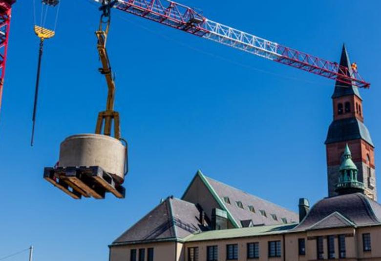 Kuvassa on oikealla kansallismuseon päärakennus ja sen torni.  Vasemmalla etualalla nostokurjen koukussa peruskivi. Taustalla on sinistä taivasta.