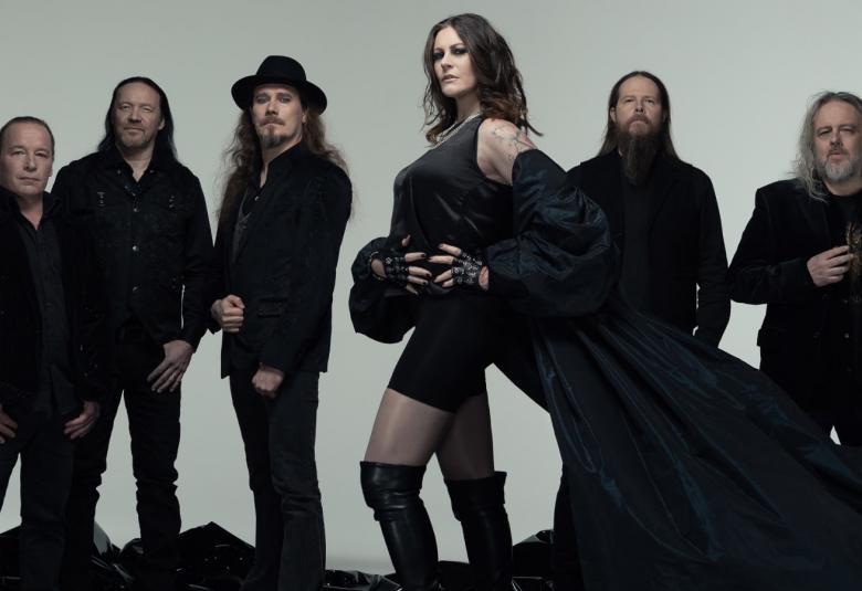 Kuvassa on seisomassa Nightwishin viisi miesjäsentä taaempana ja naisjäsen keskellä edessä. Kaikilla on mustat vaatteen päällään. Tausta on harmaa.