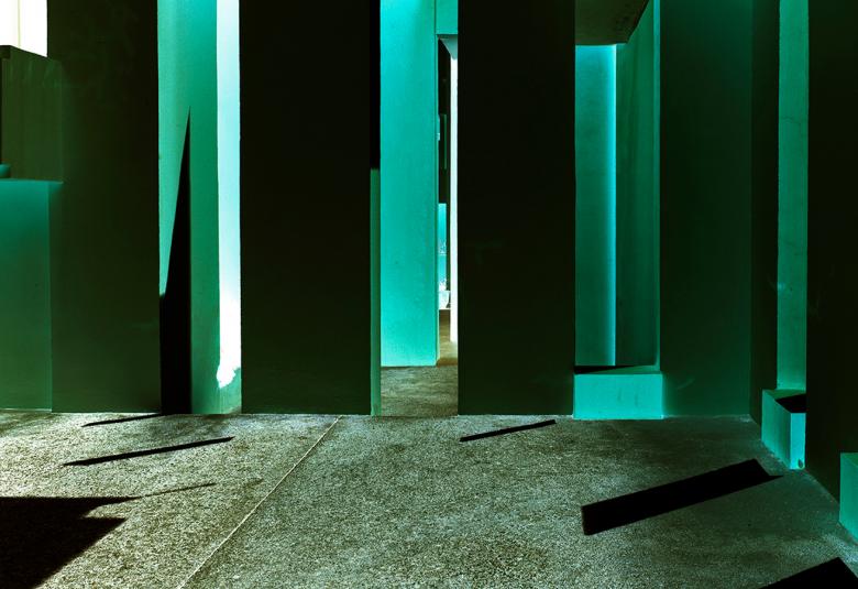 Kuvassa on Ola Kolehmaisen teos Geometric Light ja siinä on vihreitä ja mustia pylväitä  vihertävällä lattialla.  Pylväisiin osuu valoa limittäisten pylväiden väliin tulee piikkimuotoja.  Lattialla on mustaa varjoa vasemmalla.