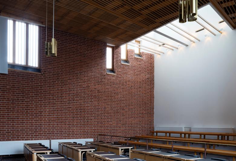 Kuvassa on Alajärven kaupungintalo ja siinä on poikittain valtuustosalipöydät.  Takana on ruskeaa tiiliseinää, jossa on ikkuna ylhäällä ja tila on korkea. Toisella seinällä on iso valkokangas.