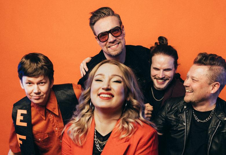 Kuvassa on East Funk Attackin viisi jäsentä puolivartalokuvassa. Heillä on mustia puseroita ja edessä olevalla naislaulajalla on oranssi jakku. Tausta on oranssi.