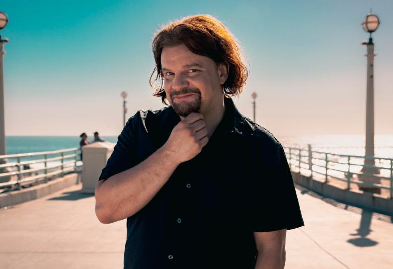 Kuvassa on Ismo Leikola seisoo kuvan keskellä mustassa t-paidassa ja oikea käsi on leualla.  Taustalla on laituri, jossa on molemmin puolin korkeat lyhtypylväät. Taustalla on meri ja sinistä taivasta.