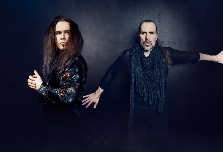 Kuvassa ovat Jarkko Ahola vasemmalla sivuttain tumman kirjavassa paidassa ja hän katsoo oikealla. Oikealla on JP Leppäluoto ja hänellä on molemmat kädet suoraan sivulla. Tausta on tumma.