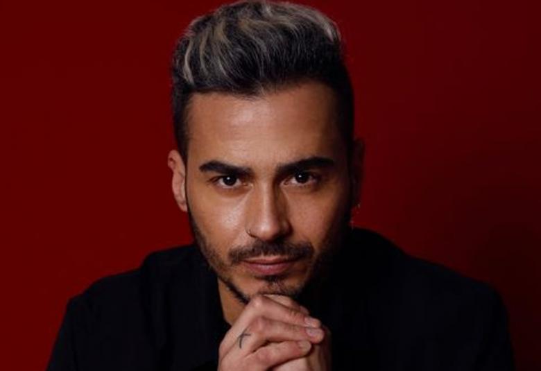 Kuvassa on Juan Debel kasvokuvassa ja hänellä on tummat, lyhyet pystyhiukset ja hieman partaa. Hänellä on kädet ristissä leuan alla.