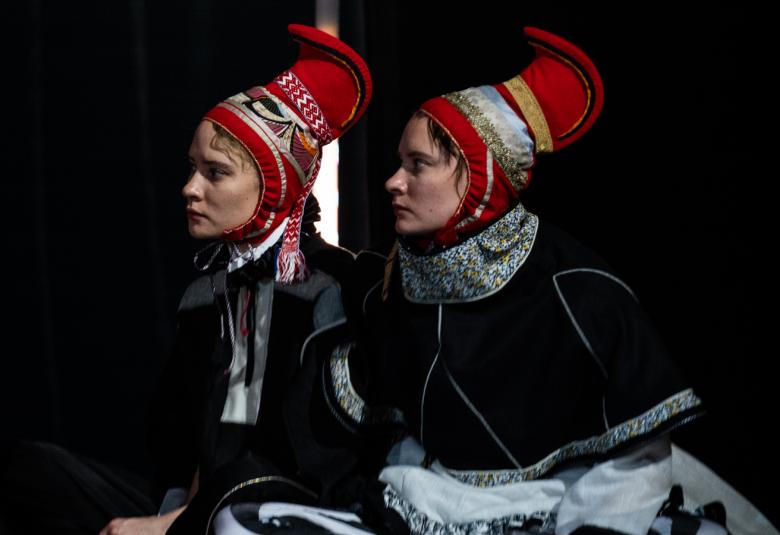 Kuvassa ovat Biret ja Gáddjá Haarla Pieski istumassa sivuttain ja heillä molemmilla on Lapin puvut päällään. Päässään heillä on punaiset osittain kirjotut Lapin hatut.