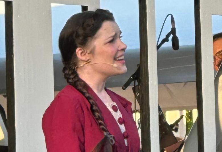 Kuvassa on keskellä sivuttain oikealle Hanna Hoikkala, jolla on tummat hiukset ja letti oikealla olkapäällä. Taistalla vaaleitä raameja, joissa oin aukkoja.