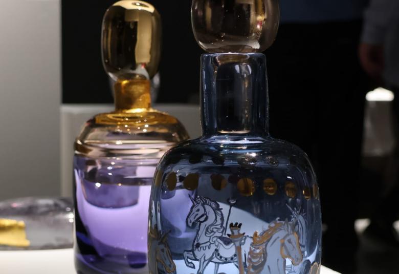 Kuvassa on kaksi lasipulloa, joissa on kultakorkit ja etummaisen pinnassa koristeellinen hevonen. Pulloissa on sinistä sävyä. 