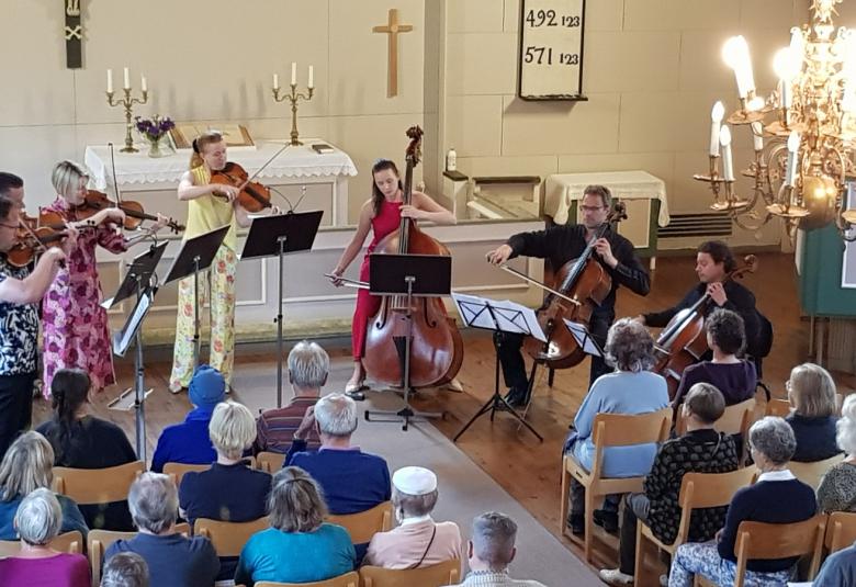 Kuvassa ovat soittajat Klamilan kirkon valkoisen alttarin ääressä.  Vasemmalla soittavat viulussa Jukka Merjanen ja Matti Koponen, alttoviulussa Eriikka Nyman punertavassa mekossa ja Kirsikka de Leval Jezierski keltaisessa housuasussa, kontrabassossa Maria Krykov punaisessa asussa ja sellossa Tuomas Ylinen ja Samuli Peltonen mustissa vaatteissa. 