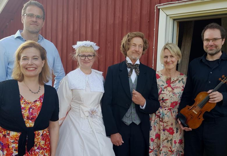 Kuvassa ovat Liisa Malmivaara edessä punakukallisessa mekossa ja takanaan Tuomas Ylinen vaalean sinisessä paidassa. Vieressä on Clara Schumann valkoisessa mekossa ja oikealla Robert Schuman mustassa frakissa ja harmaassa liivissä. Hänen vieressään on Eriikka Nylund vaaleassa punakukallisessa mekossa. Oikealla on Petteri Iivonen viulu kädessään.