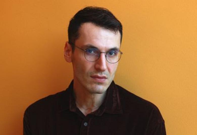 Kuvassa on Pajtim Statovci puolivartalokuvassa ja hänellä on musta pusero päällään. TAusta onn ruskehtava.