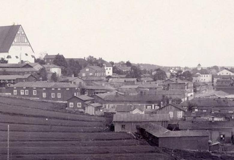 Kuvassa on näkymä, jossa on vasemmalla ylhäällä Porvoon tuomiokirkko ja alapuolella laaksossa puutaloja piharakennuksia. Kuva on musta-valkoinen.