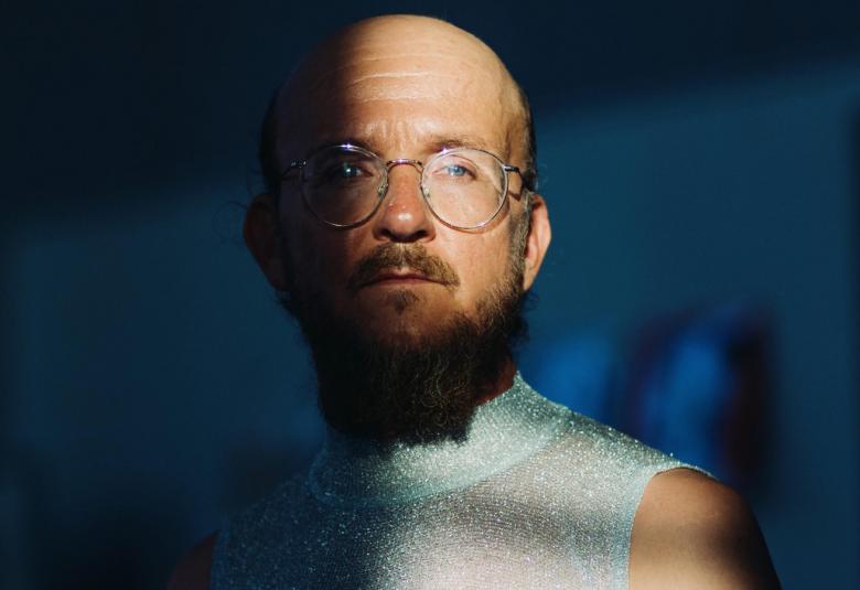 Kuvassa on Samuli Putro puolivartalokuvassa ja hänestä näkyy puolet. Vasemmalla on lähes puolet tummennettu.  Putrolla ei ole hiuksia,pyöreät ssilmälasit ja partaa.  Hänellä on valkoinen pusero päällään.