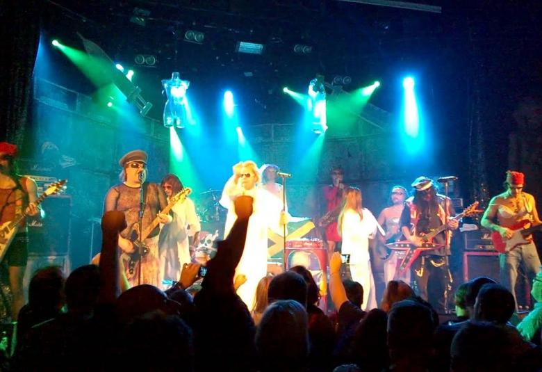 Kuvassa on Sleepy Sleepers esiintymislavalla. Vasemmalla ja oikealla ovat kitaristit ja keskellä valkoisissa puvuissa kaksi esiintyjää. Taustalla on sinistä valoa.