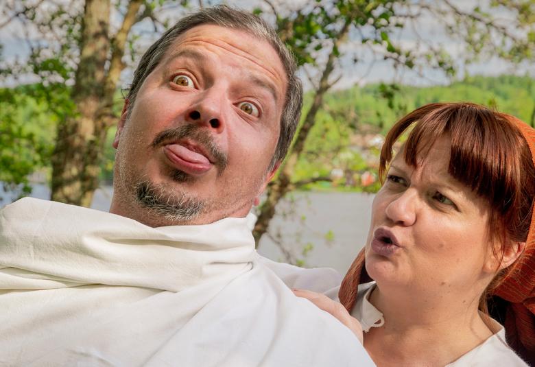  Kuvassa on vasemmalla on miehen pää, jonka ympärille on kiedottu valkoista lakanaa. Takana on ruosteen punaisessa huivissa nainen, joka pitelee lakanasta kiinni. 