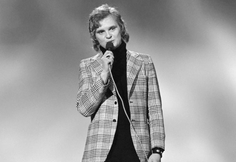 Kuvassa on Pepe Willberg seisomassa ja kuva on otettu yläviistoon. Hänellä on tumma puku päällään. Kuvan tausta on tumma.