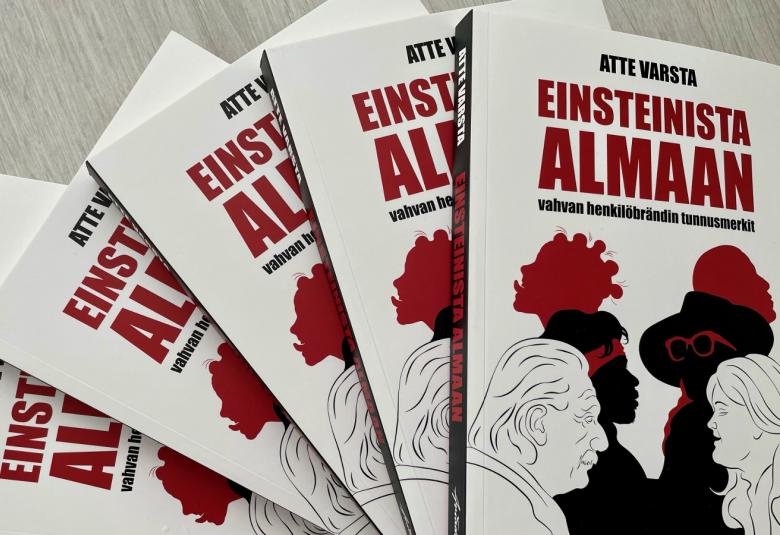 Kuvassa on viisi Einsteinista Almaan -kirjaa viuhkamaisesti.  Kannessa on kirjan nimi tumman punaisella. Alla piirroskuvat ylempänä mustat kasvot vastakkain punaisessa tukassa ja niiden alapuolella mustalla viivalla piirretyt Einsteinin ja Alman profiilit.