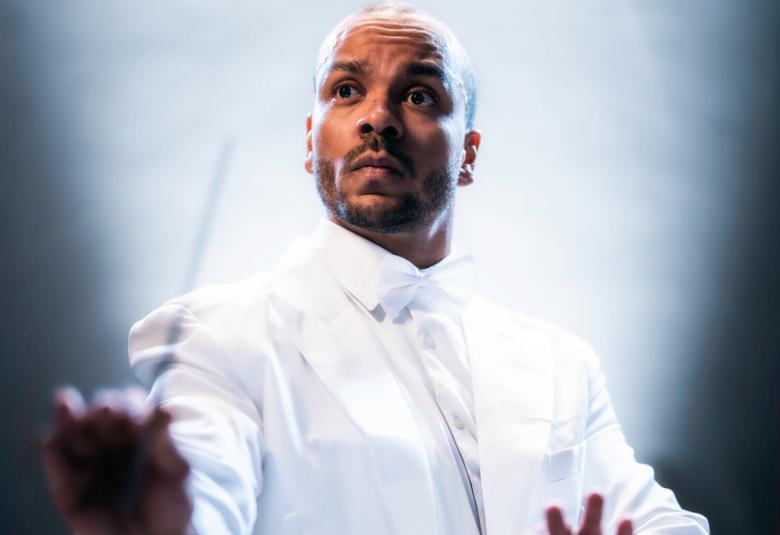  Kuvassa on Ernest Lawson valkoisessa paidassa puolivartalokuvassa tahtipuikko oikeassa kädessään. Hänellä on valkoinen takki ja paita päällään. Hänellä on vaalean ruskea iho. Tausta on kuvan molemmilta sivuilta tumman sininen ja vaalea keskeltä.