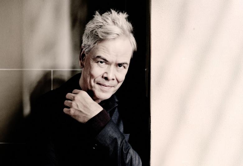 Kuvassa on Hannu Lintu vasemmalla toisessa osassa kuvaa ja siinä hän on puolivartalokuvassa mustassa takissa vasen käsi edessään.  Oikealla on kuva vaaleasta marmoriseinästä.