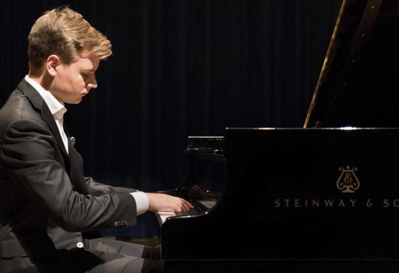 Kuvassa on Ossi Tanner sivuttain soittamassa flyygeliä mustassa puvussa.  Kuvan tausta on tumma.