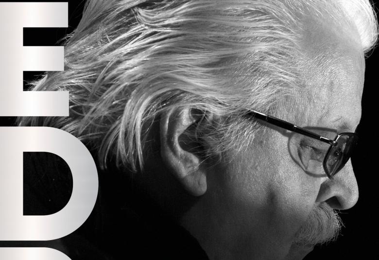 Kuvassa on Pedro Hietasen sivukuva osittain ja hänellä on vaaleat hiukset kammattuna taaksepäin sekä silmälasit. Ylhäältä alaspäin on isot, valkoiset kirjaimet E ja D.  Kuva on musta-valkoinen ja se on osa kirjan kannesta.