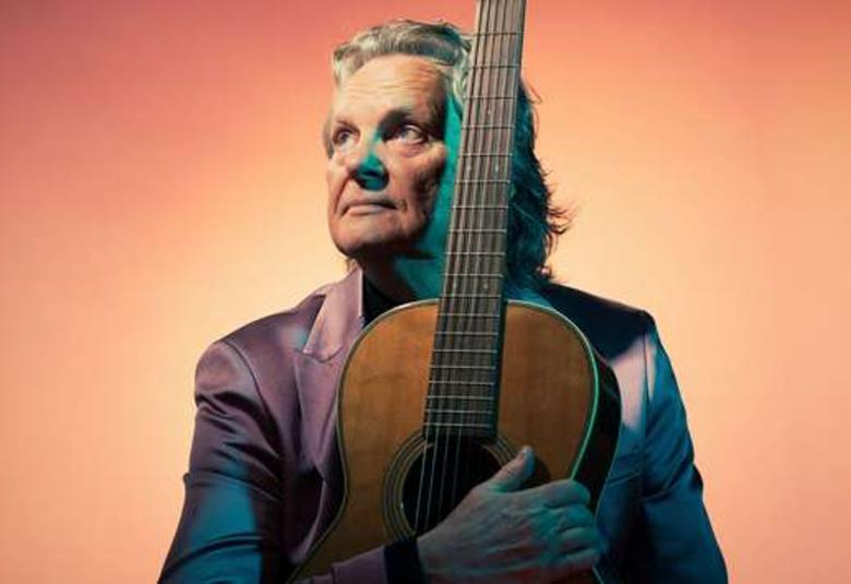 Kuvassa on Pepe Willberg istumassa kitara sylissään ja kuva on puolivartalokuva. Hänellä on katse kohotettuna vasemmalle ylöspäin. Hänellä on tumma takki päällään ja tausta on oranssi.