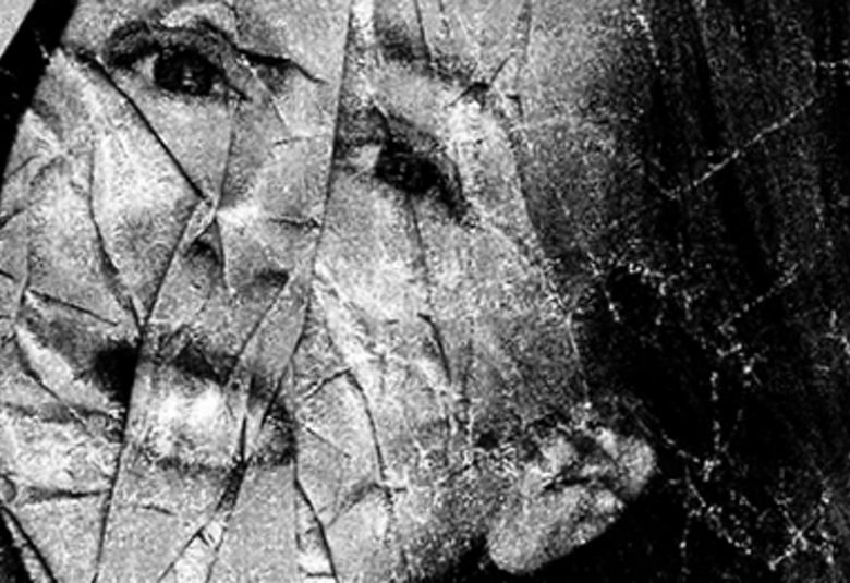 Kuvassa on nuoren naisen kasvot vinosti ja ne näkyvät rikkinäisen peilin läpi. Kuva on musta-valkoinen.