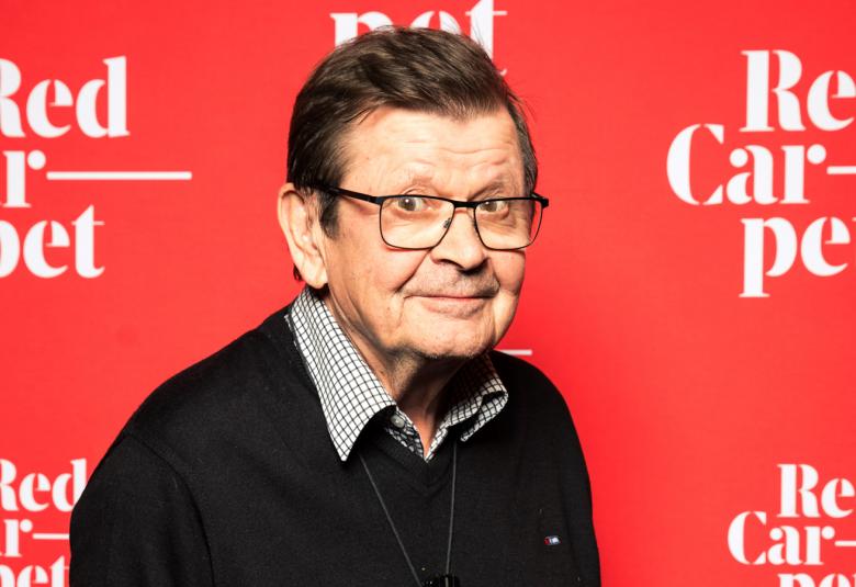 Kuvassa on Heikki Kinnunen puolivartalokuvassa ja hänellä on musta paita ja kaulupaita. Taustalla on punaisella pohjalla useaan kertaan Red Carpet eri kohdissa.