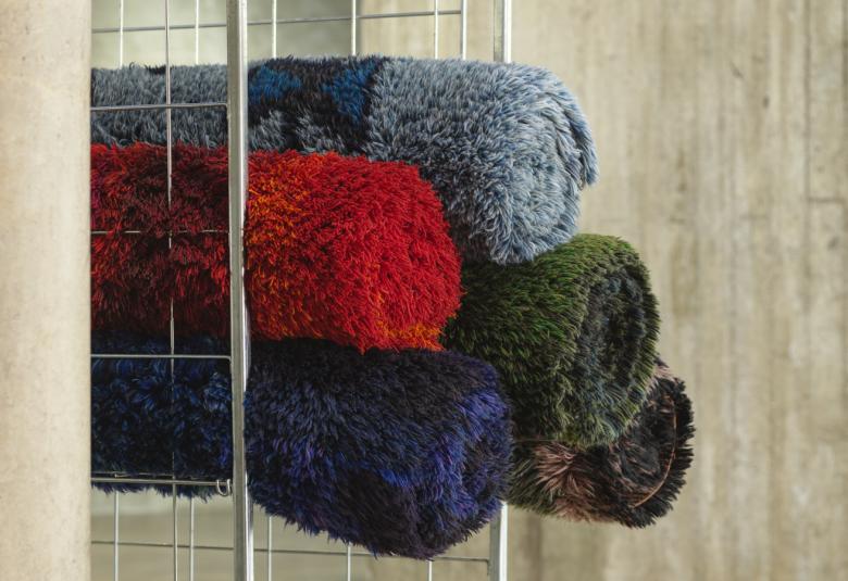 Kuvassa on vaalean pylvään takana rullakon hyllyllä olevat rullalle käärityt ryijyt. Niitä on neljä ja värit ovat tumman punainen, harmaa, tumman sininen ja tumman vihreä.