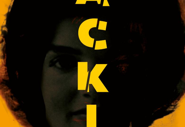 Kuvassa on tumma kasvokuva Jackie Kennedysta ja siinä näkyvät himmeästi kasvot tummien hiusten ympäröimänä. keskellä on nimi Jackie isoilla keltaisilla kirjaimilla.  Tausta on oranssi.