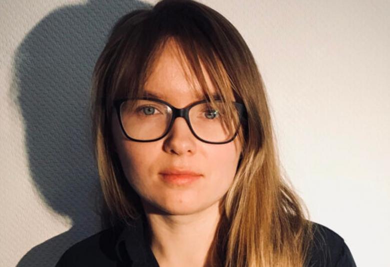 Kuvassa on Jevhenia Kuznjetsova kasvokuvassa. Hänellä on ruskeat puolipitkät hiukset ja isot silmälasit.  Taustalla näkyy hänen varjonsa vaalealla seinällä.