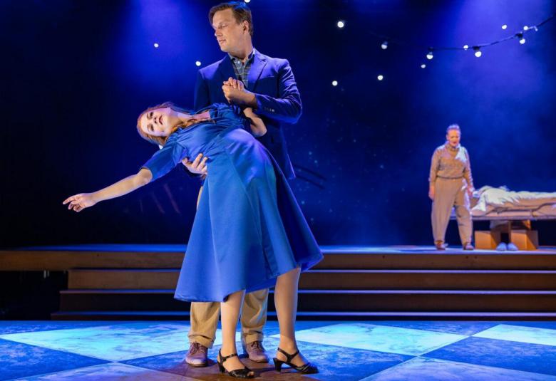 Kuvassa on tanssiva pari ja nainen on taivuttamassa taaksepäin sinisessä mekossa. Miehellä on sininen puku.  Taustalla on tumman sinisiä taivasta ja kaksi tähteä.  Kuvassa on keskellä mies oikea käsi ojennettuna ja hänellä vaalea paita ja t-paita sekä siniset far