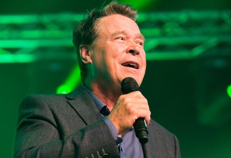 Kuvassa on Markku Aro puolivartalokuvassa kuvattuna yläviistoon ja mikki oikeassa kädessään.  Taustalla on vaakasuorassa kirkkaan vihreää ledvalastusta.