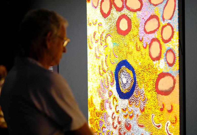 Kuvassa on hämärävalaistuksessa oleva katselija vasemmalla. Oikealla on teos, jossa on keltaista pisaramaista pintaa ja ruskeita rinkuloita ylhäällä sekä sininen renkula keskellä.