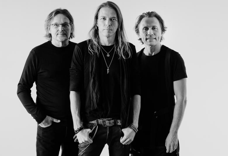 Kuvassa ovat bändin kolme jäsentä ja keskellä seisoo Eicca Toppinen. Kaikilla on mustat vaatteet. Kuva on musta-valkoinen.