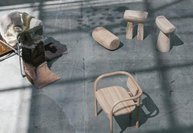 Kuvassa on harmaalla lattialla, johon osuu valoa, kalusteita.  Vasemmassa yläkulmassa on metallisella tuolilla harmaita karvamattoja.  Keskellä ylhäällä on muotoiltuja, vaaleita puupölkkyjä. Alempana on vaalea muotoiltu puutarhatuoli.  