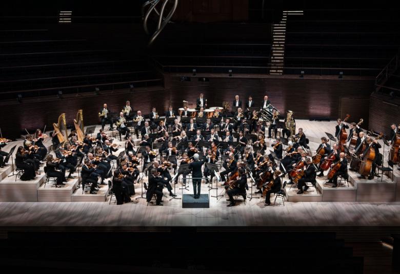 Kuvassa on Helsingin kaupunginorkesteri ylhäältä päin kuvattuna lavalla soikion muotoisesti. Jukka-Pekka Saraste on selin orkesterin edessä.
