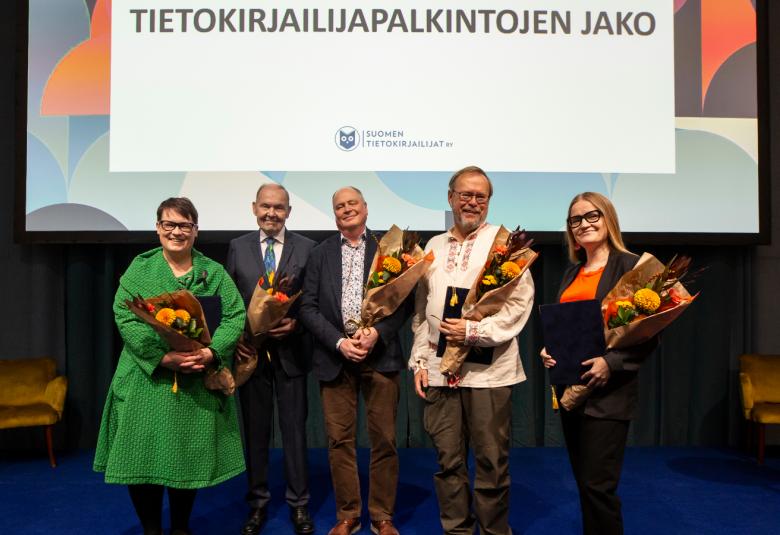 Kuvassa ovat Anu Lahtinen, Risto Niku, Pasi Saukkonen, Seppo Vuokko ja Johanna Vehkoo seisomassa palkintokukat kädessään. Taustalla on kultti, jossa lukee tietokirjapalkintojen jako isolla näytöllä.