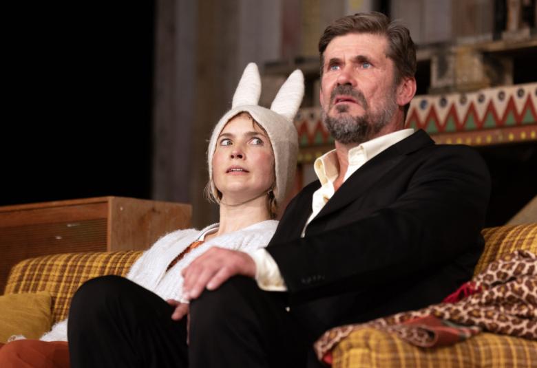 Kuvassa on sohvalla istumassa vasemmalla puolella jäniksen asussa valkoisiss pupukorvissa Marja Salo ja oikealla Tommi Korpela mustassa puvussa. 