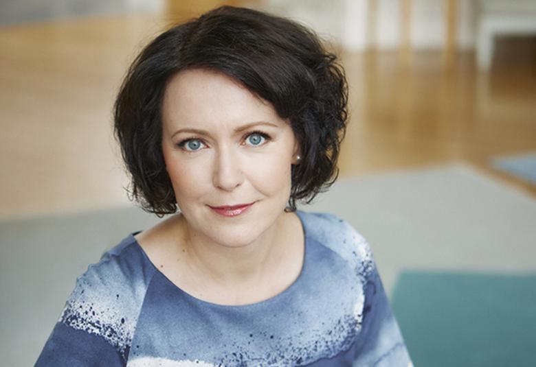 Kuvassa on Jenni Haukio puolivartalokuvassa ja hänellä on sini-valko harmaa mekko ja kuosi on taivaansinimäinen. Haukiolla on tummat puolipitkät hiukset.