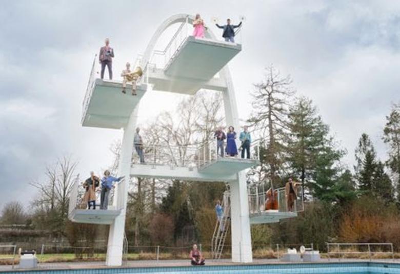 Kuvassa on valkoinen uimahyppyteline ja siinä on yhtyeen jäseniä seisomassa eri neljällä telineellä sekä yksi maassa. Taustalla on metsää ja harmaata pilveä.