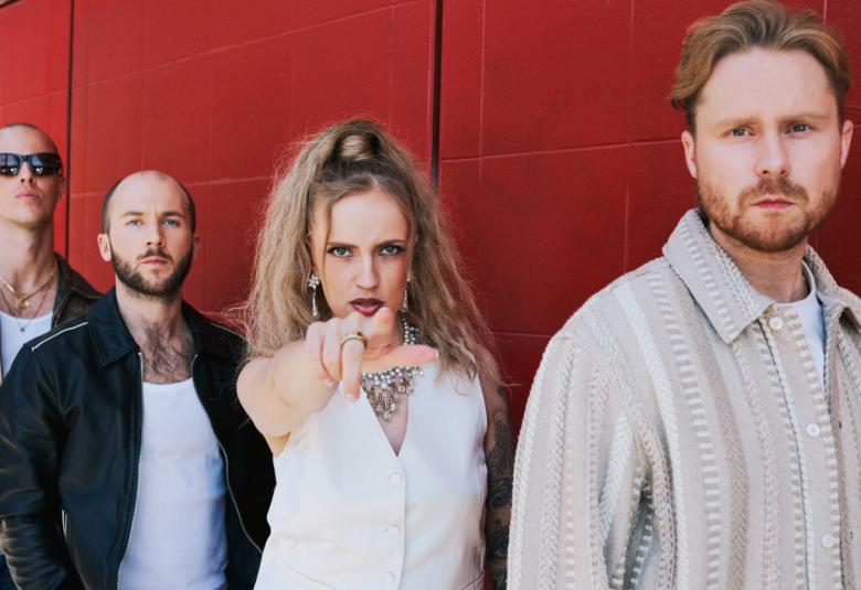 Kuvassa ovat Haloo Helsingin neljä jäsentä. Taaimmaisella miehellä vasemmalla on kulunut nahkatakki ja aurinkolasit sejö seuraavalla musta pusakka. Hänen vieressään on naisjäsen valkoisessa, hihattomassa puserossa ja hän osoittaa oikealla kädellään eteenpäin.  Hänen edessään seisoo mies, jolla on vaalea villatakki. Kuva on puolivartalokuva. Tausta on punaruskea.