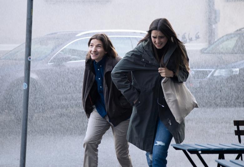 Kuvassa ovat Elias Westerberg ja Linnea Leino kävelemässä sateessa ja tuulessa kaupungin kadulla. Taustalla näkyy autoja.